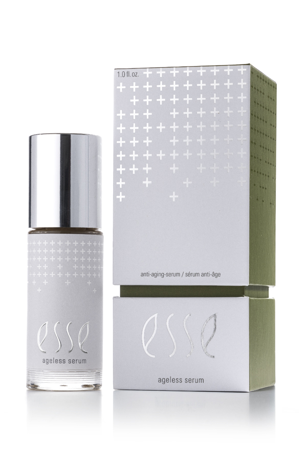 A bottle of Esse Ageless Serum with a silver cap stands beside its matching box, both displaying a minimalist white and silver design with cross patterns and product text.
