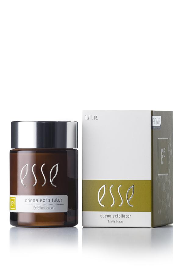 A brown container of Esse Cocoa Exfoliator, featuring a black lid and white text, is placed next to its product box. The box is white with green detailing and matching white text, displaying the same information as the container.