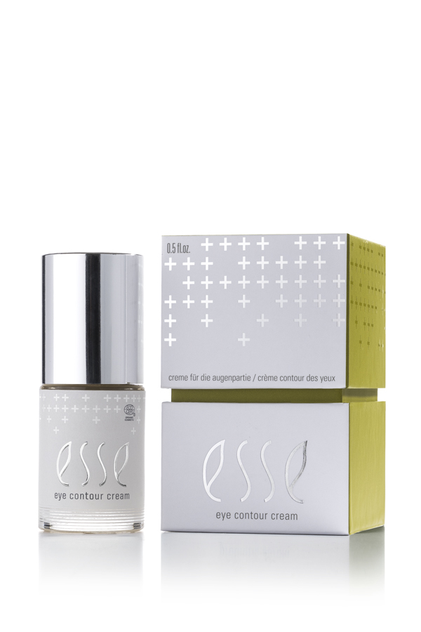 A bottle of Esse Eye Contour Cream with a silver cap is displayed beside its white and green box, both decorated with minimalist text and plus sign motifs.