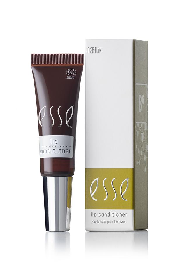 An Esse Lip Conditioner tube sits beside its open, partially-visible packaging. The dark brown tube features a silver cap and white text that reads "Esse Lip Conditioner". Its box displays yellow and white sections with the same text and a B6 symbol.