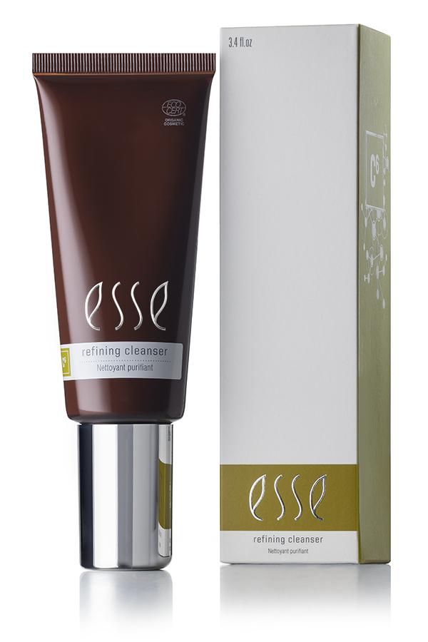 A dark brown tube and a matching box of Esse Refining Cleanser are displayed. The box is white with green accents showcasing the product label. The tube features a shiny silver cap and contains 3.4 fl oz of the Esse Refining Cleanser.