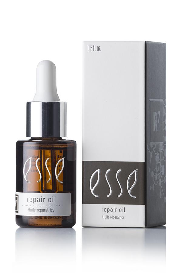 A brown glass dropper bottle of Esse Repair Oil stands next to its corresponding white and gray box packaging. The label on both the bottle and the box reads "Esse Repair Oil - Huile réparatrice." The bottle has a silver cap and a white dropper.