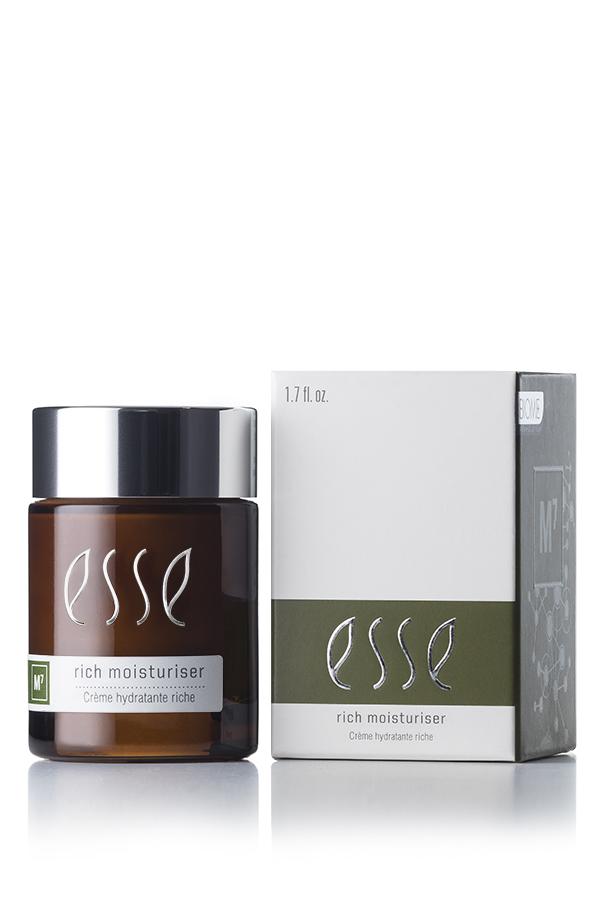 A jar of Esse Rich Moisturiser is displayed beside its packaging. The jar is dark brown, topped with a sleek black lid and adorned with white text. Its accompanying white box showcases the brand logo and product name prominently, highlighted by a green accent stripe near the bottom that includes additional information.