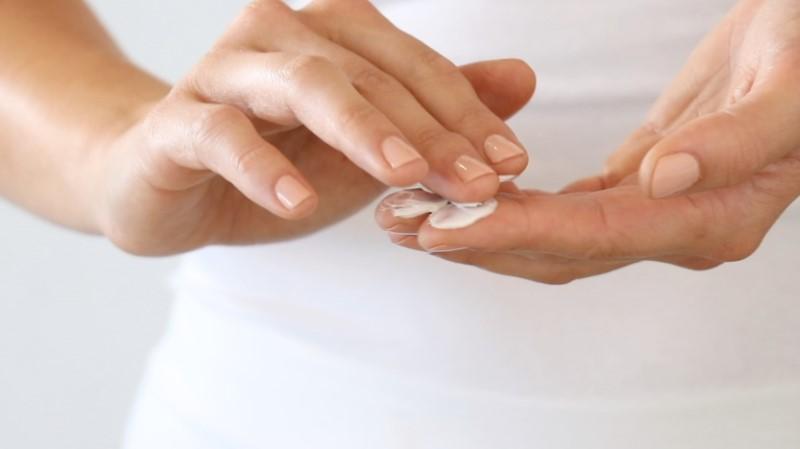In a close-up image, a person with neatly manicured nails is gently applying Esse Nourish Moisturiser to their fingertips. The background is a soft, light color, possibly white or light gray. The focus is solely on the person's hands and the soothing application of the moisturiser.