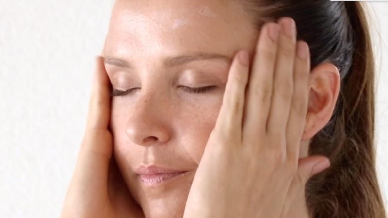 A person with closed eyes gently pressing hands against the sides of their face, appearing to be in a state of relaxation or skin care routine with Esse Restorative Moisturiser. The background is plain and light-colored.