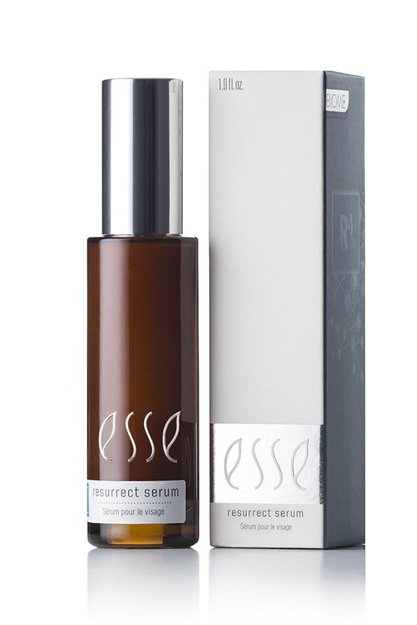 A brown bottle of Esse Resurrect Serum stands beside its white and gray packaging box. The bottle is equipped with a silver pump cap, and the label displays "Esse Resurrect Serum" along with "Serum pour le Visage." The same text also appears on the packaging.