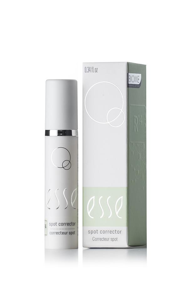 A compact, white bottle of Esse Spot Corrector is showcased beside its coordinating box. Both the bottle and the box boast minimalist designs, adorned with the brand name "esse" in an elegant, lowercase script and circular geometric elements. The box also includes additional text and a light green panel.