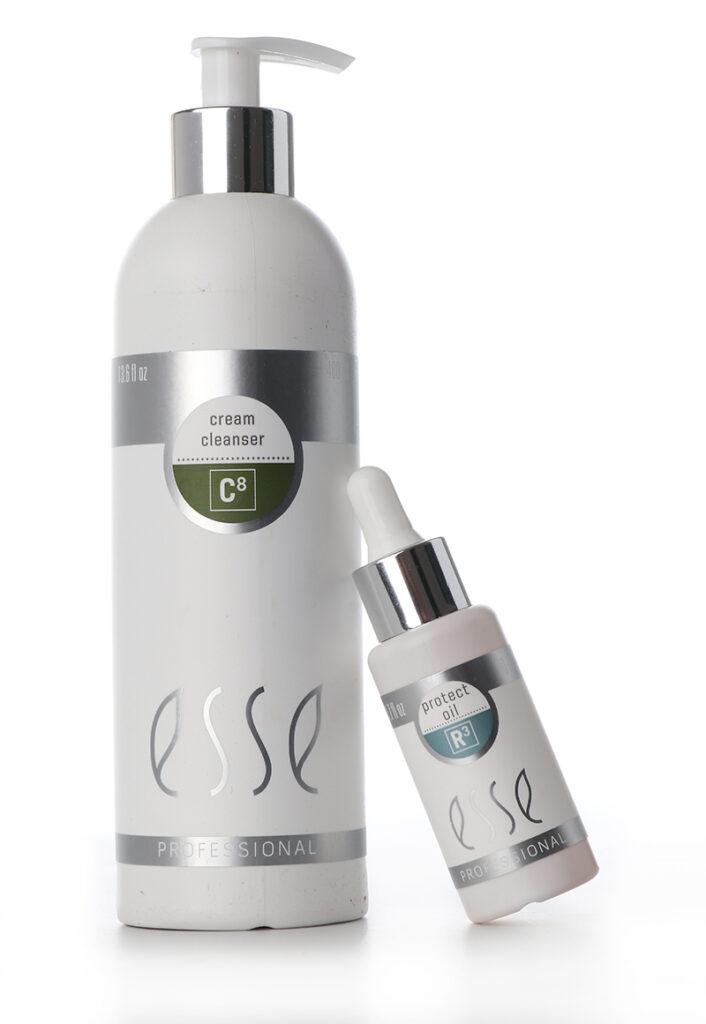 A white pump bottle labeled "esse Professional Cream Cleanser," positioned next to a small white dropper bottle labeled "Protect Oil." Both bottles feature a minimalist design with silver accents and gray fonts. The cleanser bottle is significantly larger.