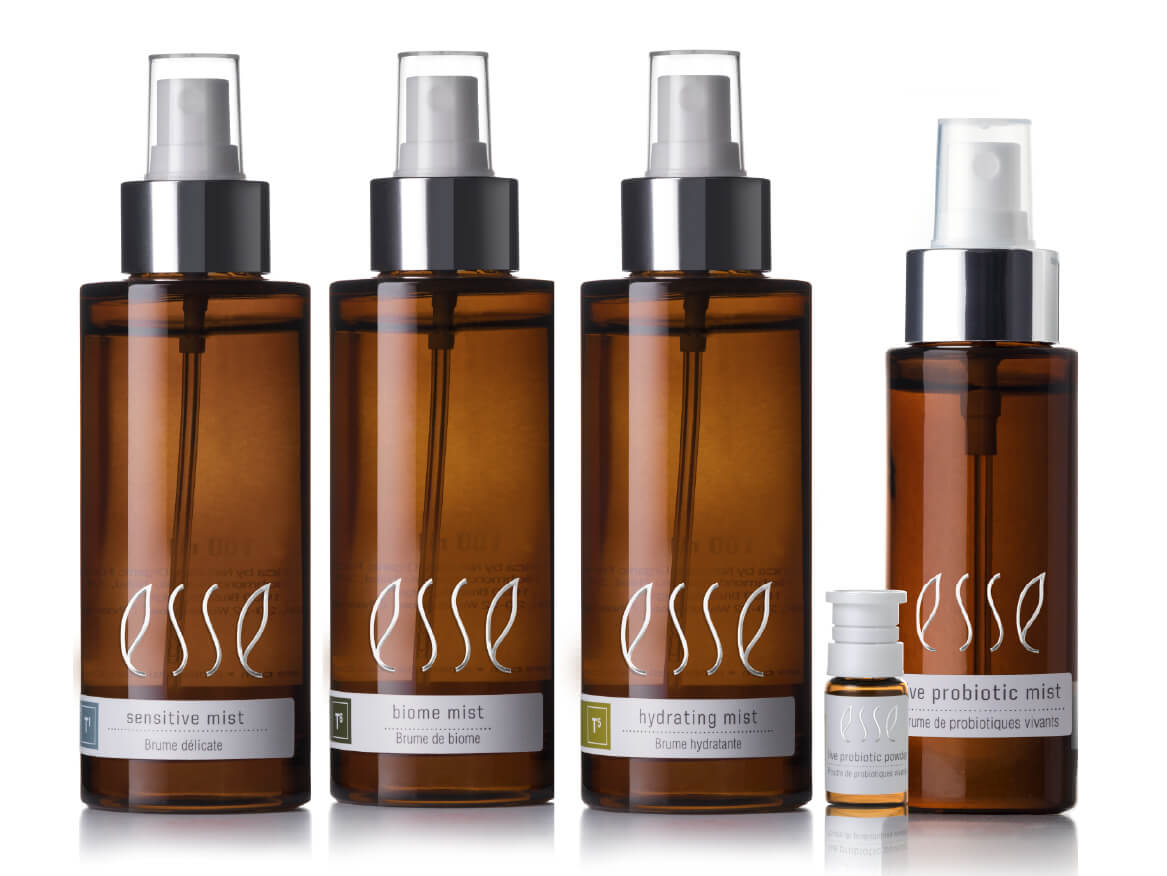 Discover the Esse Mist range: Four amber spray bottles labeled “esse” stand in a row—Sensitive Mist, Biome Mist, Hydrating Mist, and Live Probiotic Mist. A small vial sits in front of the last bottle.