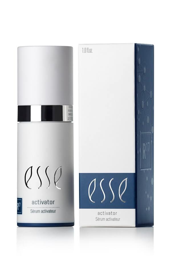 A bottle and box of Esse Activator are shown. The white bottle has a silver band and blue label, while the white box features blue accents and the text "esse activator Sérum activateur.